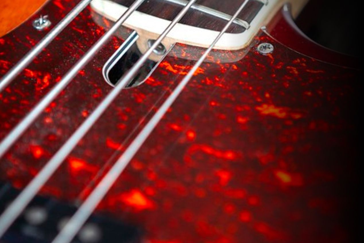 Primo piano delle corde e del corpo di un basso elettrico con finitura rosso fiammante, immagine simbolo del Corso di Basso Elettrico alla Scuola e Accademia di Musica Cluster